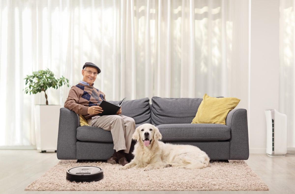 elderly man sitting on couch in livingroom with golden retreiver on the carpet